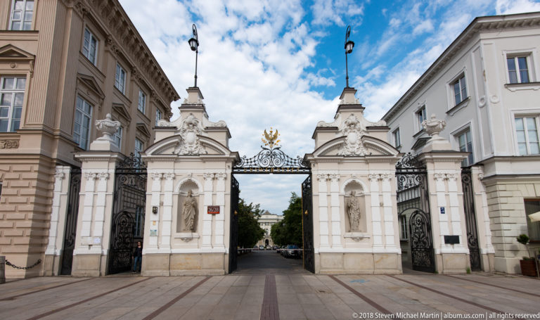 University of Warsaw main gate with white sculpted pylons, wrought iron, and crowned eagle crest.