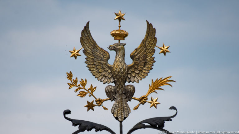Gilded crowned Polish eagle with spread wings and stars mounted above the University of Warsaw gate.
