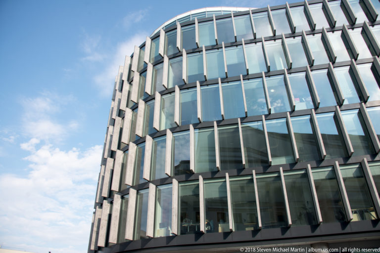 Low-angle view of a curved modern glass building with closely spaced projecting vertical fins.