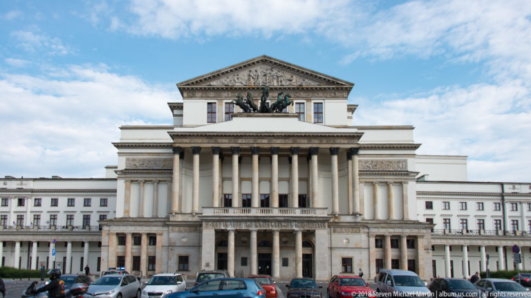 Grand Theatre in Warsaw with tall central columns, sculptural pediment, and cars parked along the street.