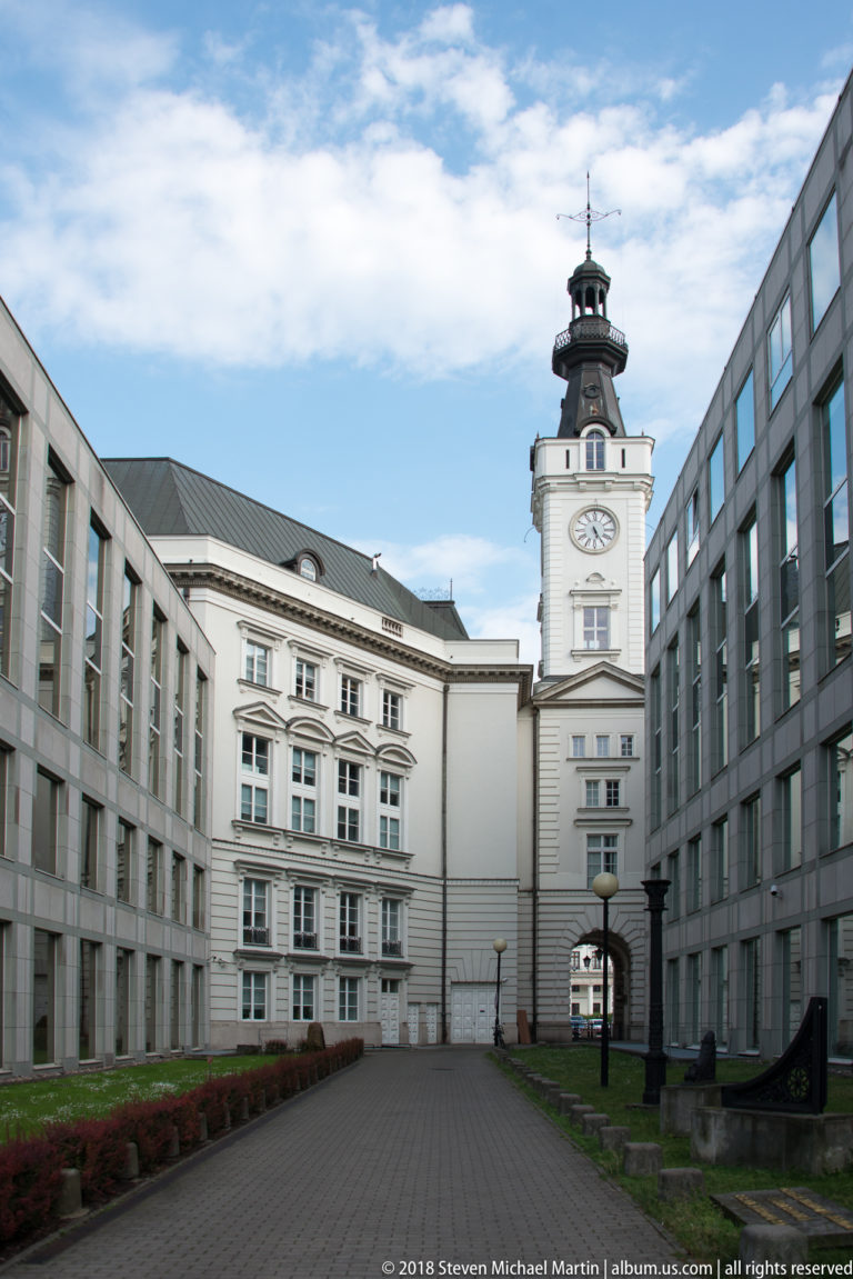 Courtyard framed by modern wings leading to a white historic building with a clock tower and lantern.