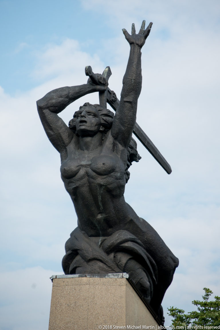 Bronze Nike figure raises one arm and holds a sword against the sky at the Monument to the Heroes of Warsaw.