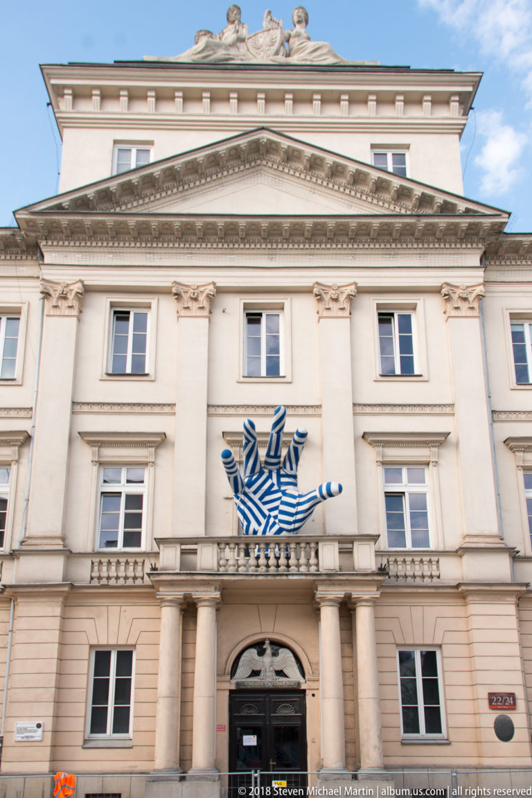 Neoclassical cream facade with central columns, triangular pediment, and a large blue-and-white emblem above the entrance.