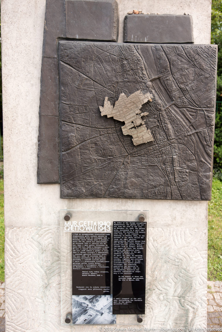Dark metal memorial plaque with raised relief map and text mounted on a pale stone base.