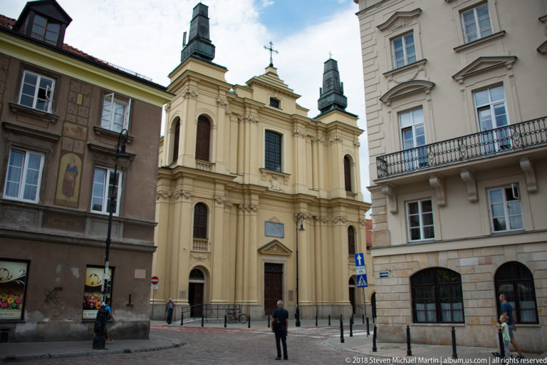 Cream Baroque Church of the Holy Spirit with twin towers and pilastered facade between taller Warsaw buildings.