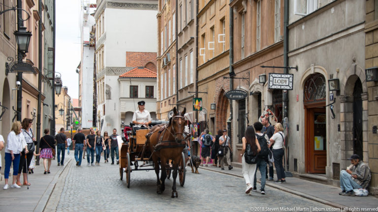 Horse-drawn carriage traveling through a crowded narrow Old Town street lined with historic buildings and pedestrians.