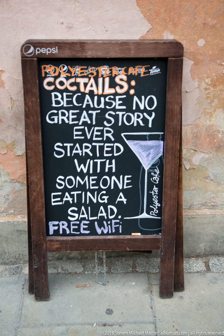 Pollyester Café chalkboard advertising cocktails with humorous text and a line drawing of a martini glass.