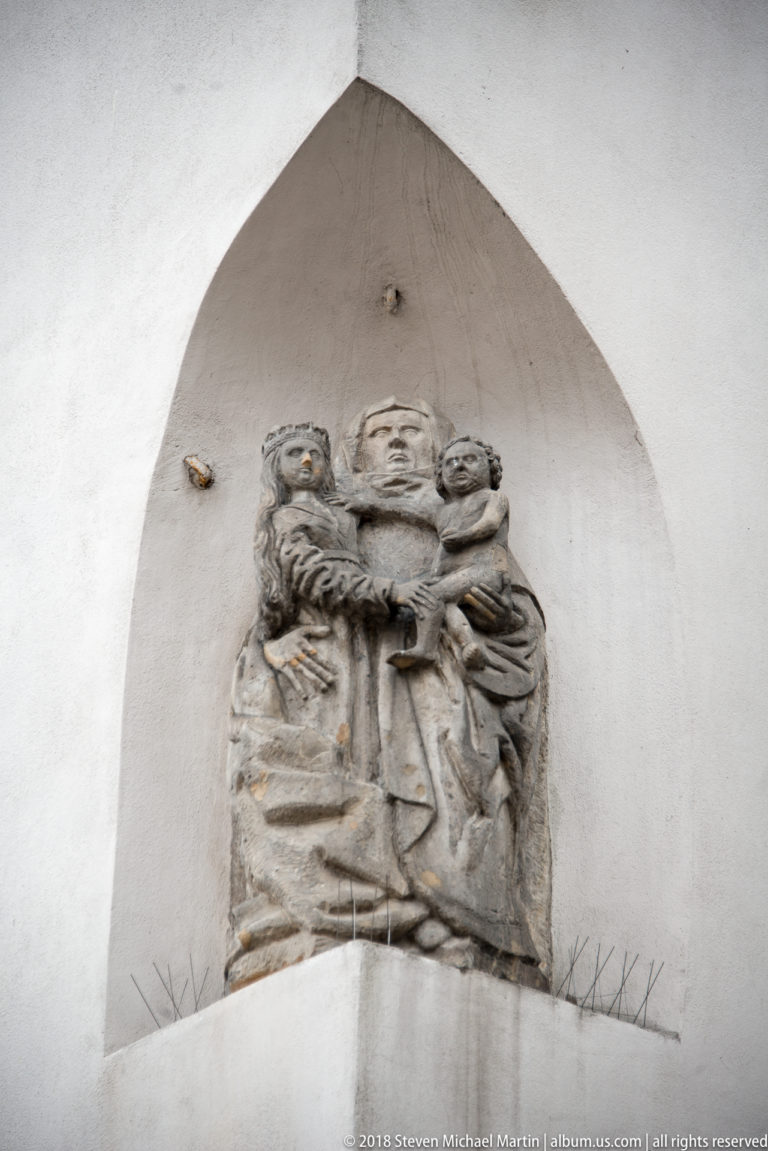 Weathered stone relief of three closely grouped human figures set high within a pointed recessed niche.