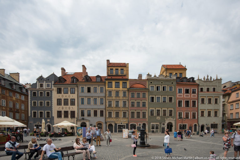Wide view across Warsaw's Old Town Market Square toward rows of colorful reconstructed townhouses and visitors.