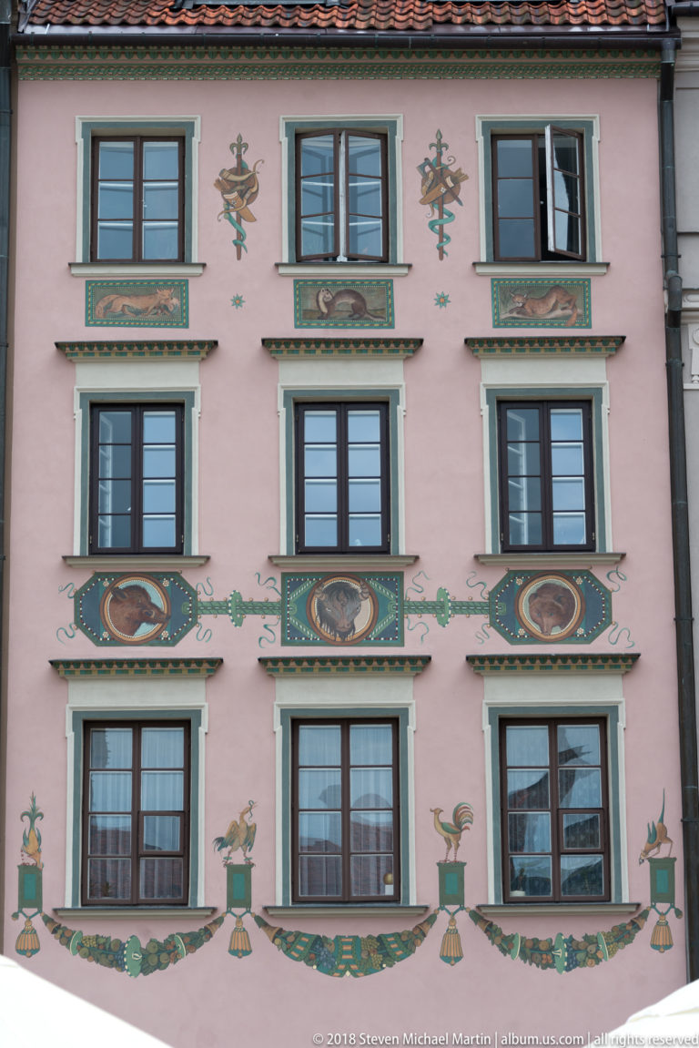 Pink Old Town townhouse with painted birds, floral ornament, portrait medallions, and rows of dark-framed windows.