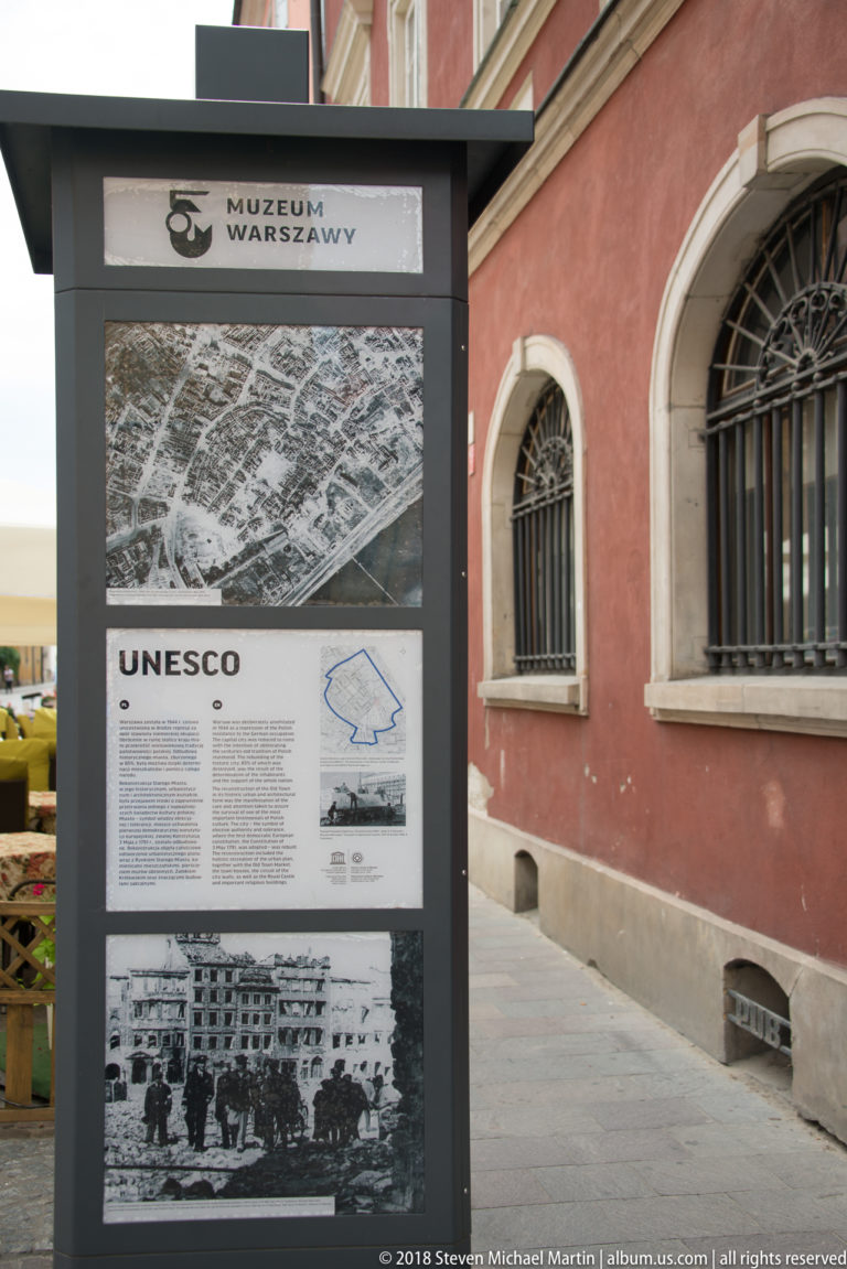 Freestanding UNESCO interpretation panel beside a red building, with aerial photograph, text, map, and historic images.