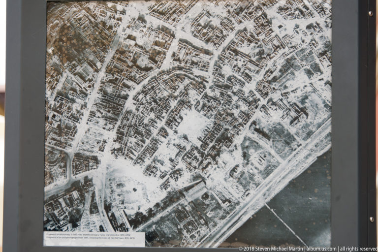 Black-and-white aerial photograph of heavily damaged urban blocks displayed on an interpretive panel in Warsaw.