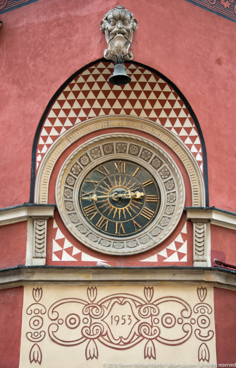 Decorative Roman-numeral clock above an ornamental facade panel visibly dated 1953.
