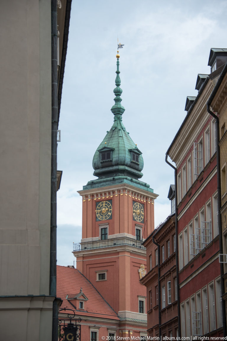 Royal Castle clock tower with green copper roof framed between historic Old Town buildings.