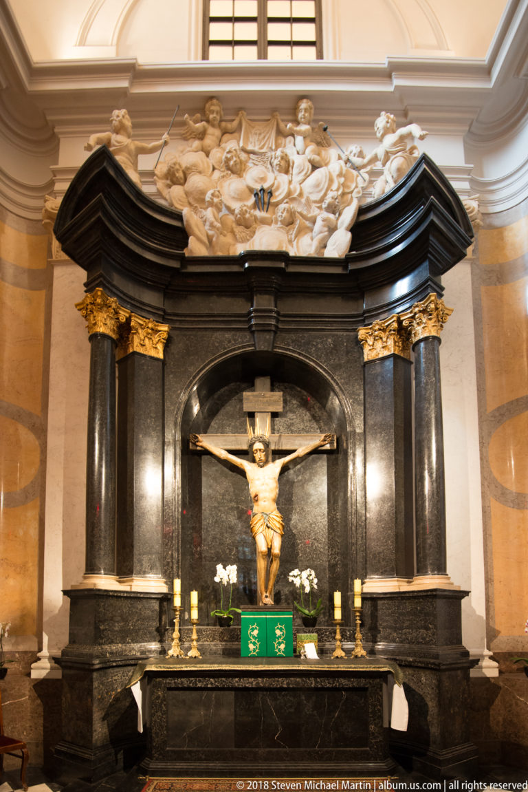Crucifix above an altar framed by black marble columns, gold capitals, and pale sculpted figures.
