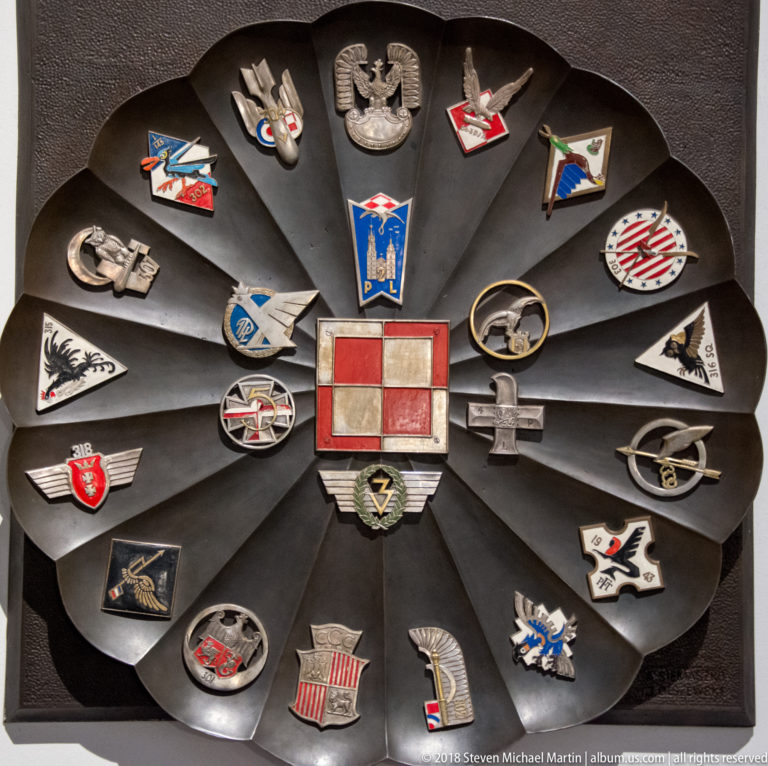 Radial display of Polish military and aviation badges with eagles, wings, shields, and a red-and-white central emblem.