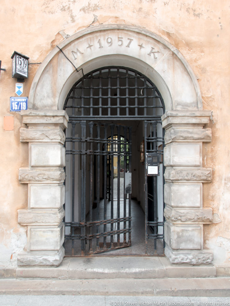 Rusticated arched gateway with iron grille, weathered plaster, street-number plaques, and a carved 1957 date.