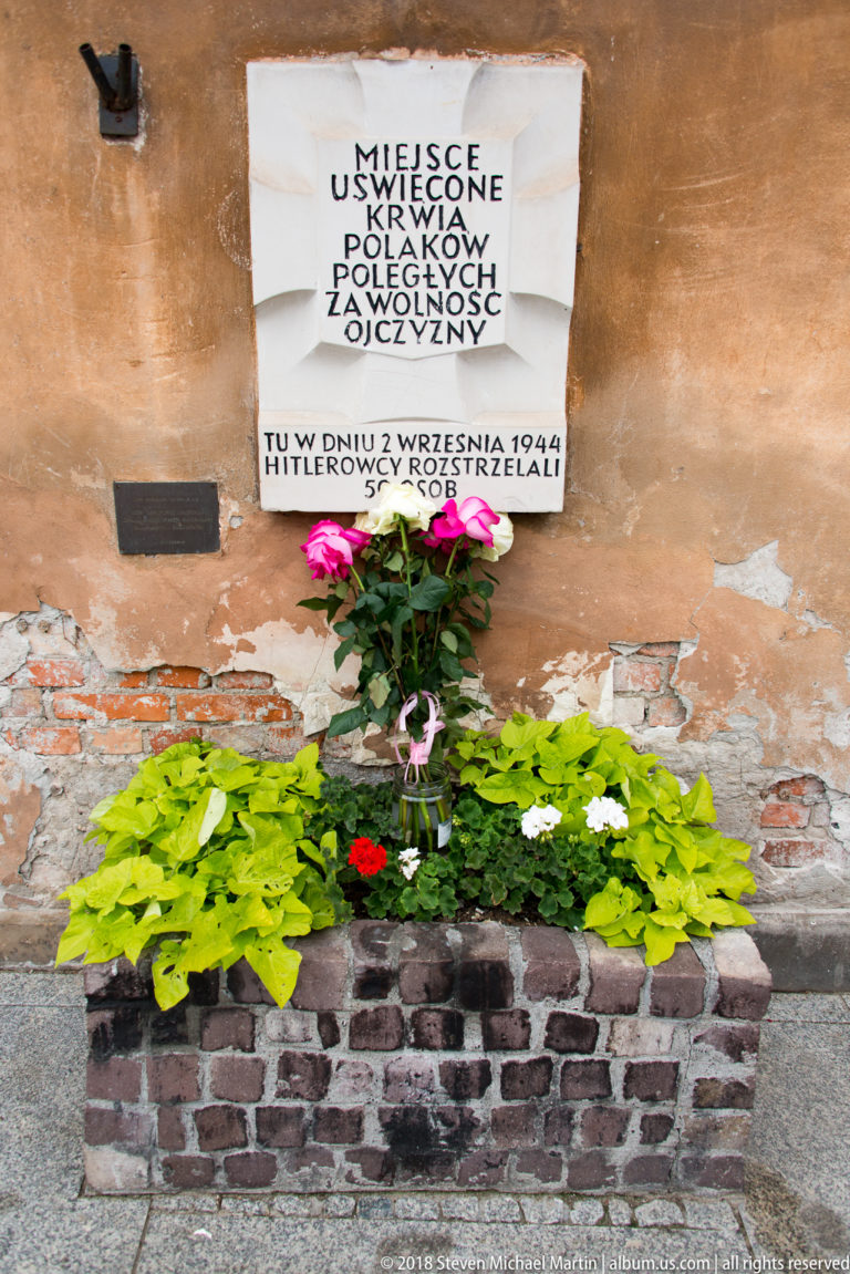 Polish World War II memorial plaque on a weathered wall above flowers, recording an execution on 2 September 1944.