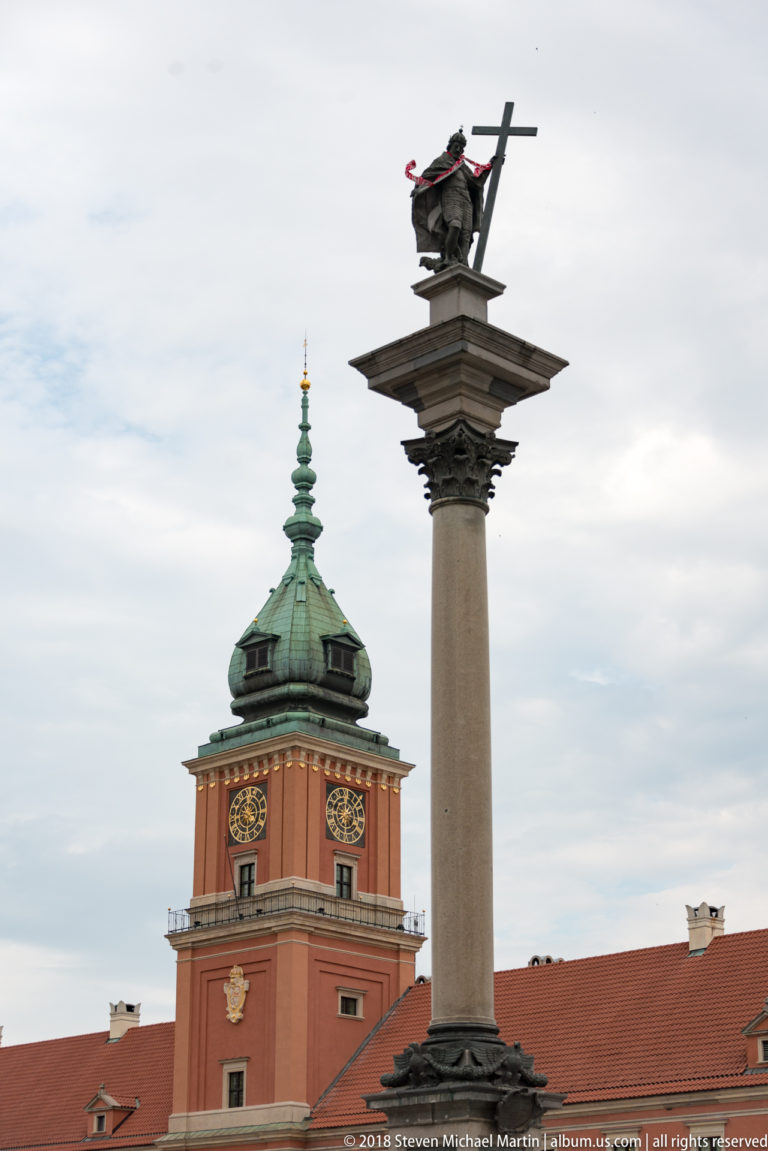 Sigismund's Column stands before the red clock tower and green copper roof of the Royal Castle in Warsaw.