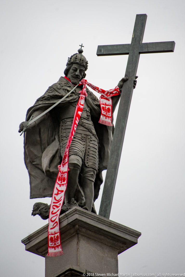 Bronze statue of Sigismund III Vasa holding a cross and sword, with red-and-white ribbons tied around the monument.