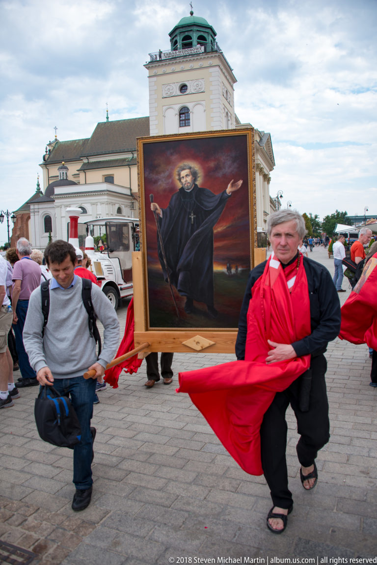 People carry a large framed religious painting wrapped with red cloth in a procession near St. Anne's Church bell tower.