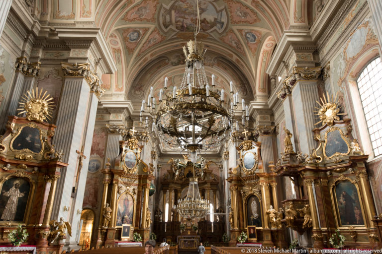 Large chandelier hangs between gilded side altars and tall pilasters beneath the painted vault of St. Anne's Church.