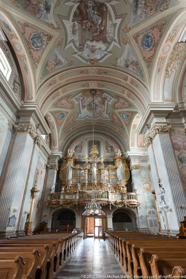 Rear view of St. Anne's Church with gilded organ loft, painted vault, tall pilasters, and wooden pews.