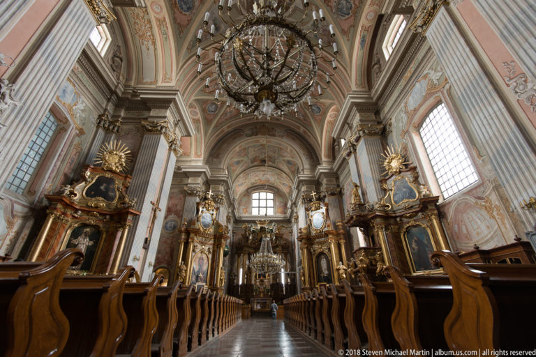 St. Anne's Church nave with wooden pews, painted vault, gilded side altars, chandelier, and high altar.