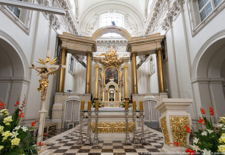 Carmelite Church sanctuary with monumental high altar, tall columns, gilded ornament, flowers, and checkered floor.
