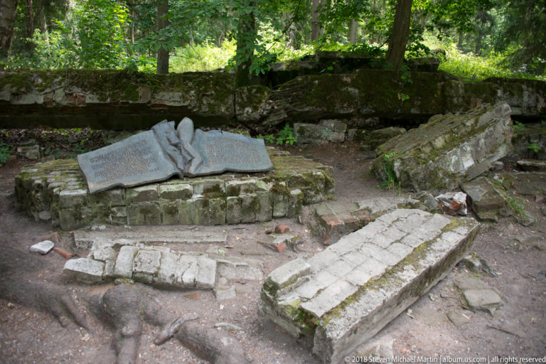 Stone memorial shaped like an open book on a low base, surrounded by broken masonry and mossy ruins.