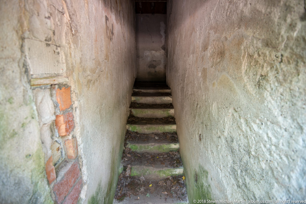 Narrow worn steps ascending between rough concrete walls, with exposed red brick along the damaged left side.