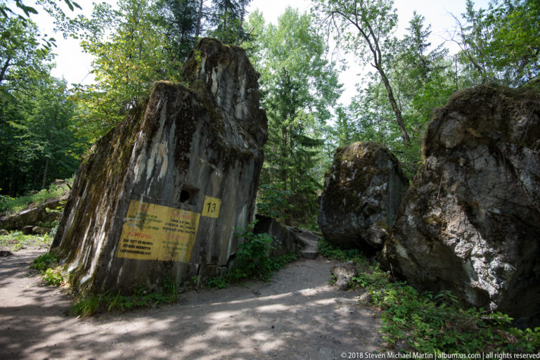 Towering broken concrete slabs marked 13 forming a narrow passage through bunker ruins in woodland.