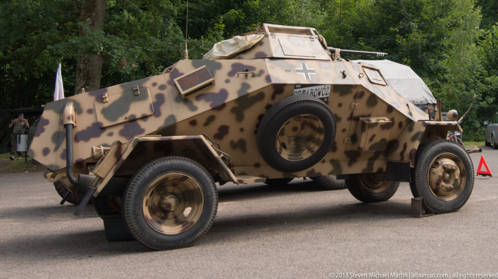 Camouflaged German armored reconnaissance vehicle with angular hull, wheels, spare tire, and black-and-white cross displayed outdoors.