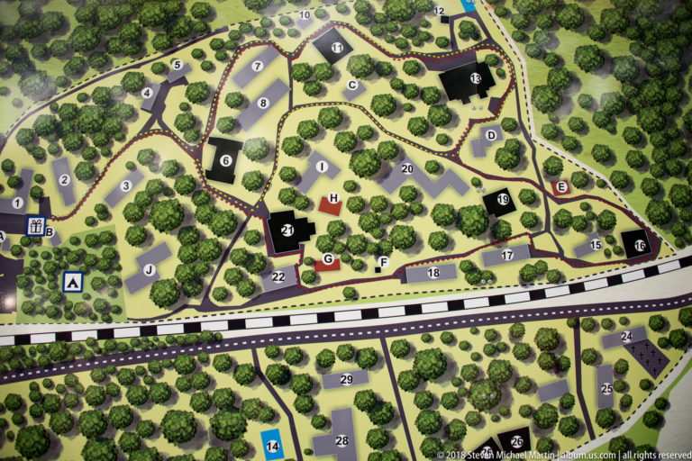 Illustrated Wolf’s Lair site map with numbered buildings, paths, roads, railway line, and dense surrounding woodland.