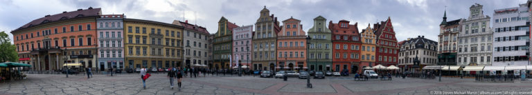 Colorful narrow townhouses with ornate gables line Wrocław Market Square above pedestrians and café seating.