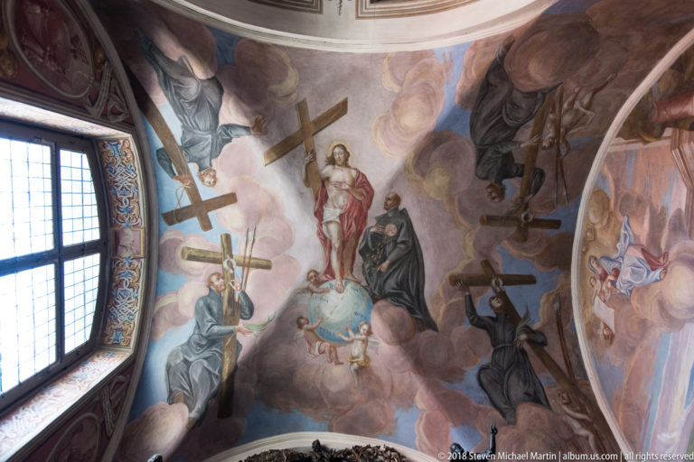 Baroque vault fresco with a central sacred figure, attendants, several large crosses, clouds, and a window at left.