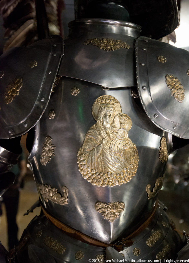 Close view of blackened plate armor decorated with a gilded Virgin-and-Child medallion and smaller gilt ornaments.