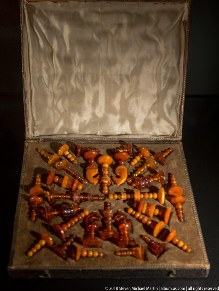Open display case filled with amber necklaces, pendants, beads, and carved ornaments in yellow, orange, and reddish-brown tones.