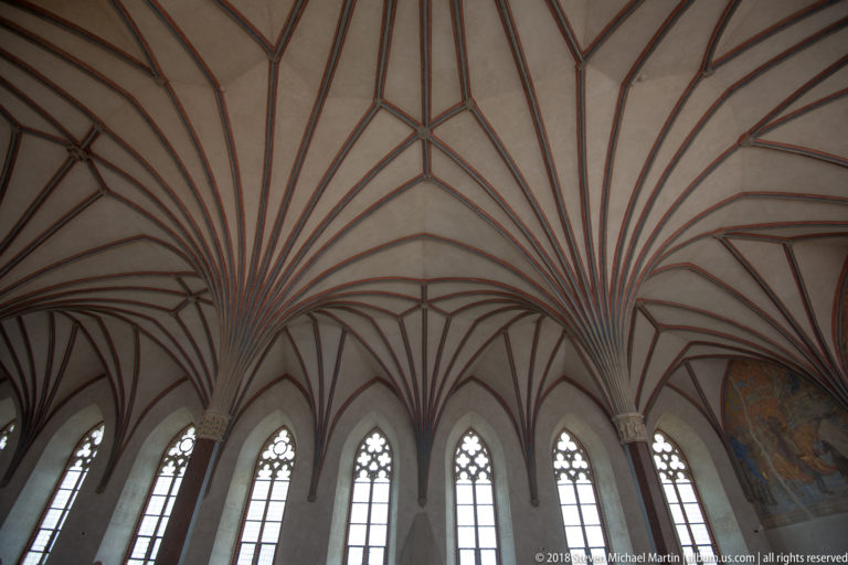 Upward view of fan-like Gothic rib vaulting above a row of tall pointed traceried windows.