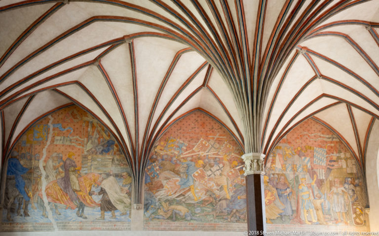 Three large medieval narrative murals with figures, horses, banners, and architecture beneath pointed Gothic vaults.