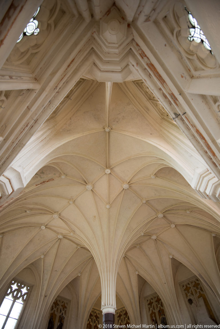 Close upward view of pale Gothic ribs converging at carved bosses beneath layered arch moldings with traces of red paint.