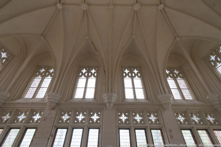 Group of tall Gothic windows with intricate pale tracery beneath converging rib vaults.