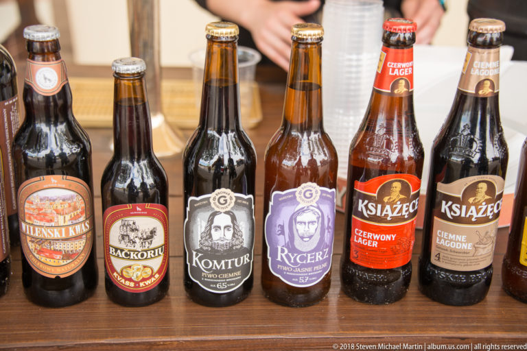 Row of assorted bottled beers with colorful Polish labels featuring portraits, heraldic motifs, and medieval-themed names.