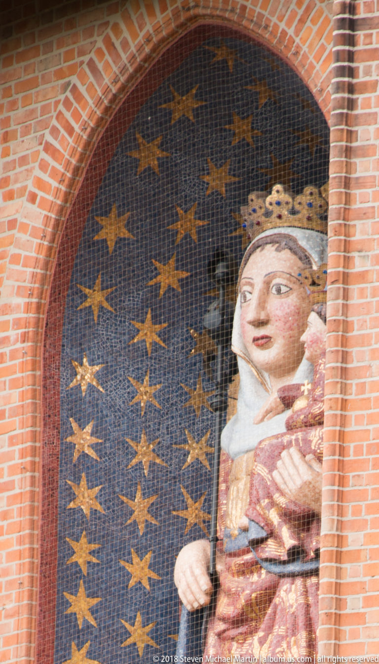Monumental mosaic of the crowned Virgin and Child against a star-filled blue background within a red-brick arched niche.