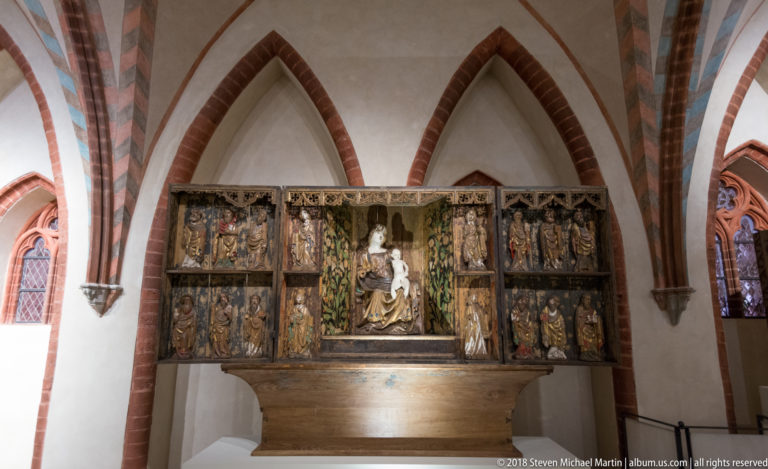 Large multi-panel Gothic altarpiece with a central seated Virgin and Child surrounded by smaller carved saints and narrative scenes.
