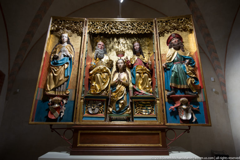 Open polychrome Gothic altarpiece with gilded tracery, enthroned central sacred figures, and standing saints on the side panels.