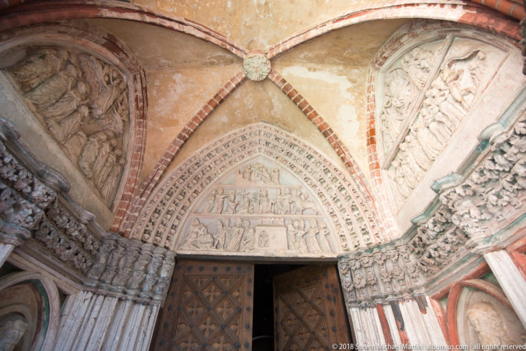 Elaborately carved Gothic portal with figurative tympanum, sculpted archivolts, standing jamb figures, and double wooden doors.