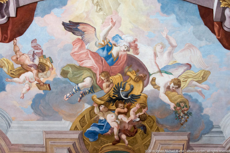 Ceiling fresco with airborne figures and putti surrounding a shield bearing a black double-headed eagle.