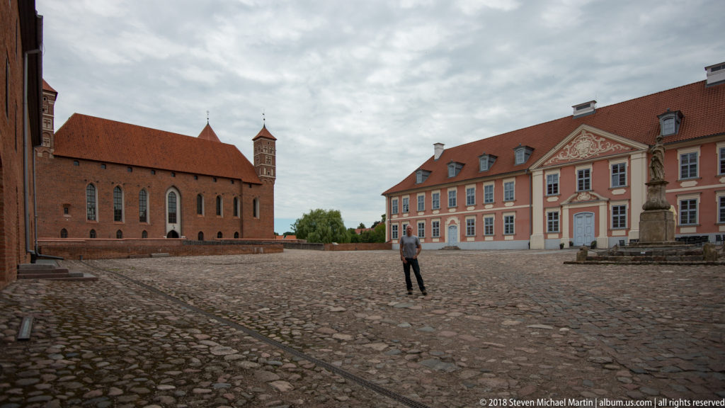 Large cobbled courtyard with red-brick castle wing on the left and long pink palace range on the right.