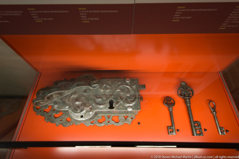 Large decorative iron lock plate and three old keys displayed side by side in a red museum case.